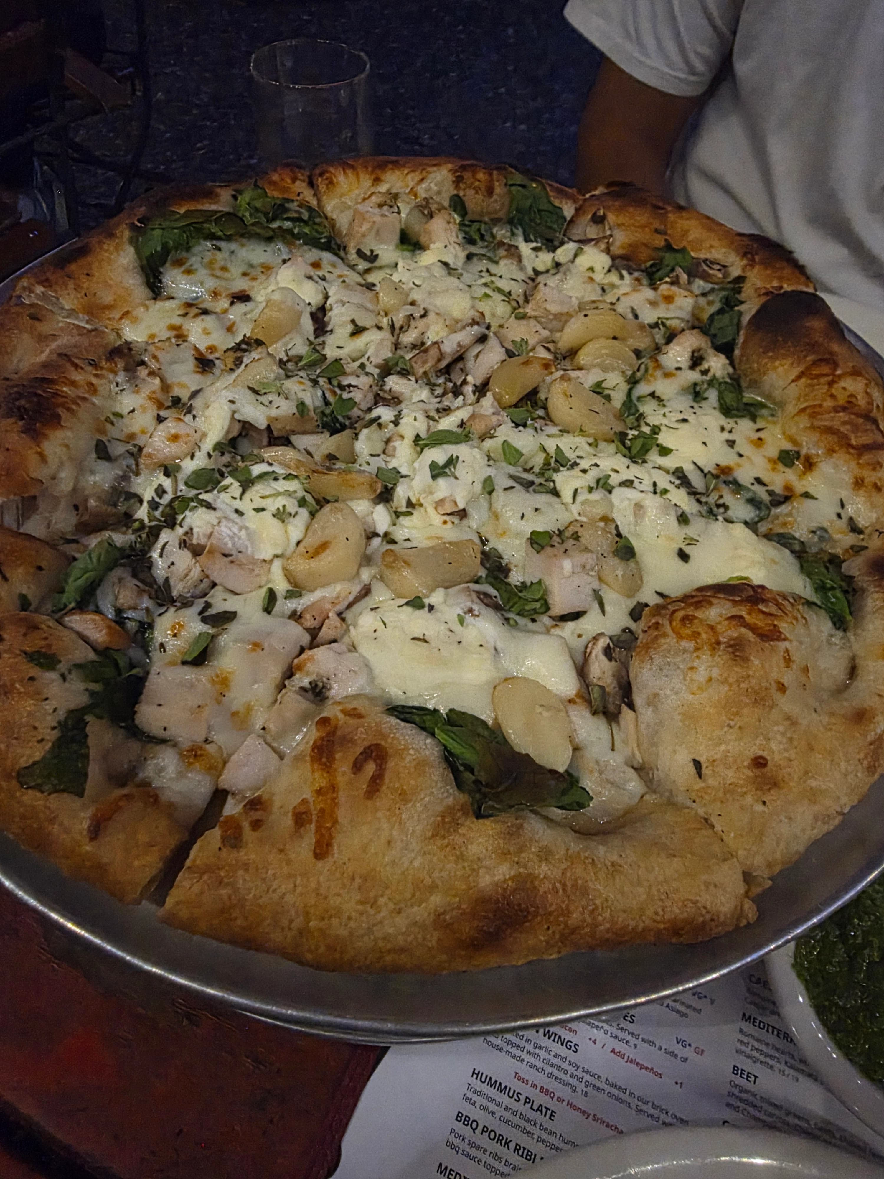 A pizza with cheese, chicken, potatoes, and spinach on a metal tray.